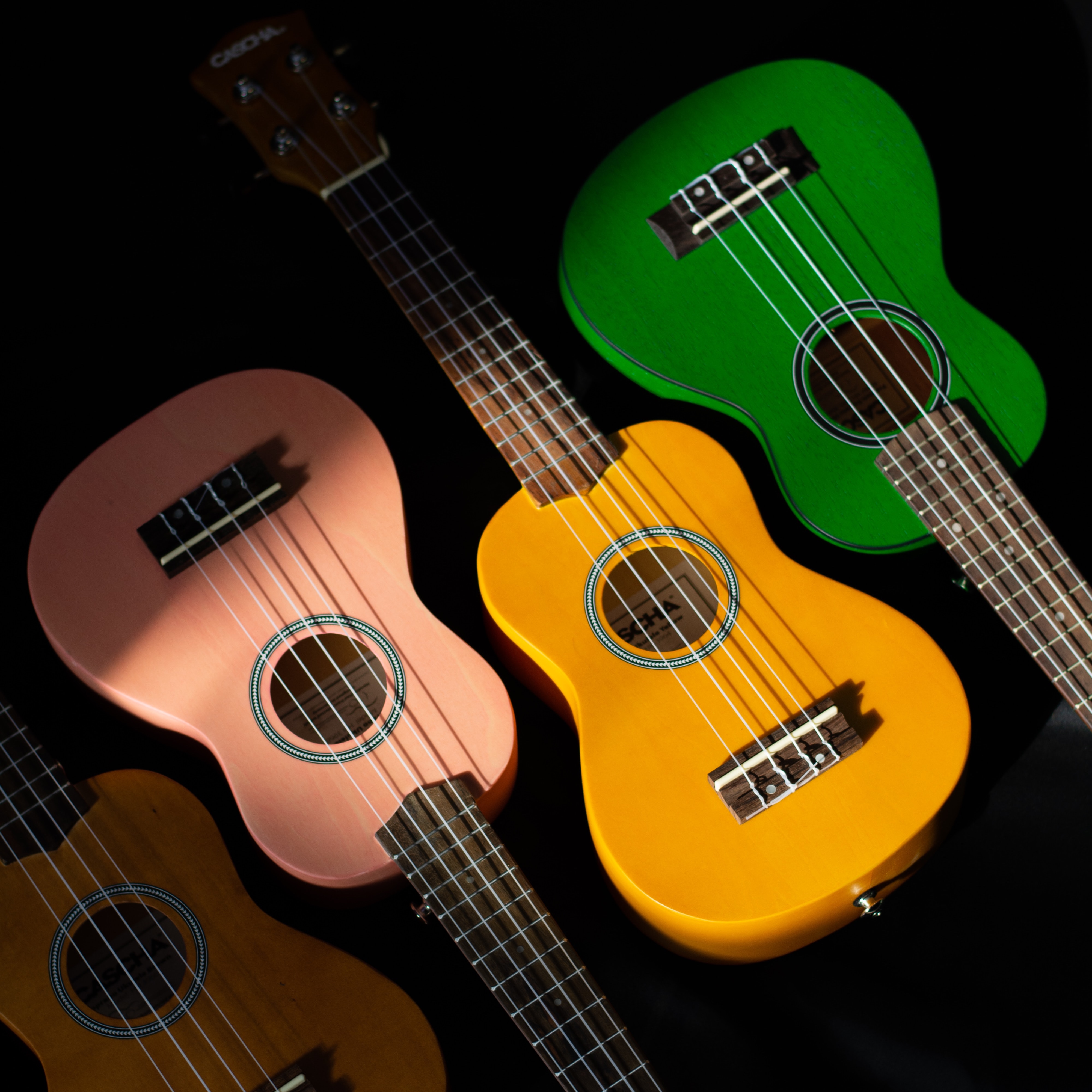 Three ukuleles in a row. one pink, one yellow, one green